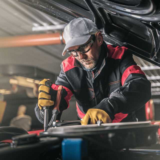 Automotive technician working on a car engine while wearing safety glasses and gloves