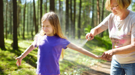 Mother spraying insect repellent on daughter's arm