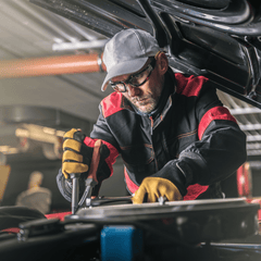 Automotive technician working on a car engine while wearing safety glasses and gloves