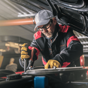 Automotive technician working on a car engine while wearing safety glasses and gloves