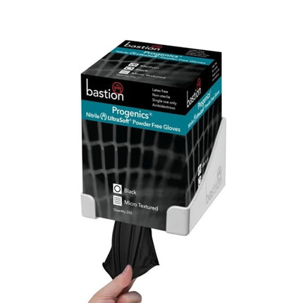 Hand pulling a black nitrile exam glove from a Bastion Progenics glove box mounted on a wall bracket for hygienic dispensing