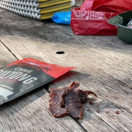 Chief Biltong Chilli flavour snack on a wooden surface with a package and other items in the background